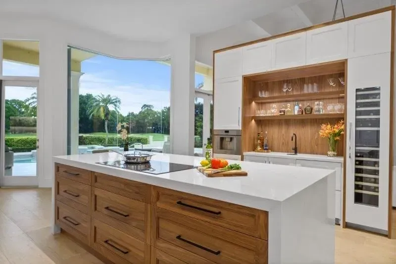 Modern kitchen with wood island, white countertops, and a view of a backyard pool through open windows