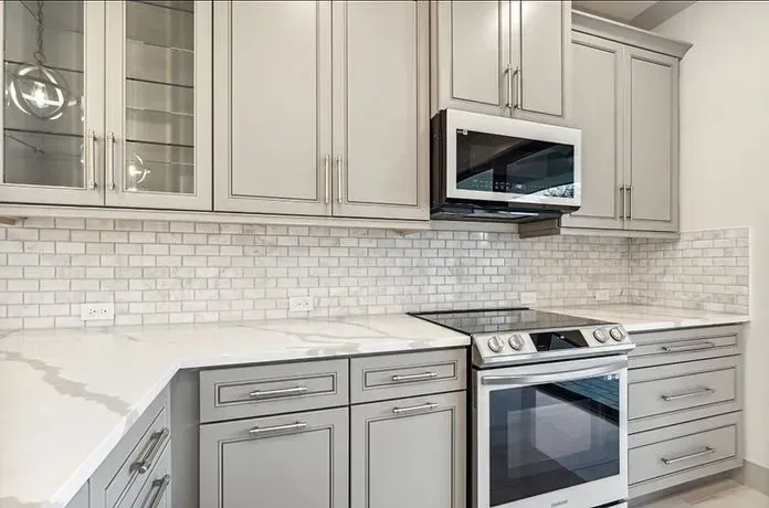 Bright modern kitchen with gray cabinets, white tile backsplash, and stainless steel stove and microwave.