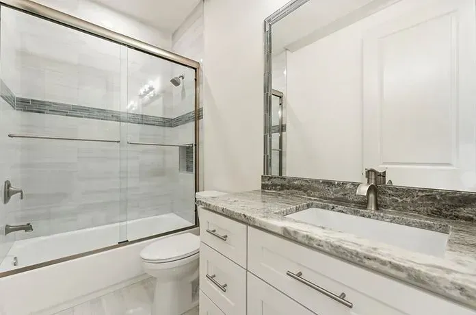 Bright white bathroom with granite vanity and a glass-enclosed bathtub/shower.