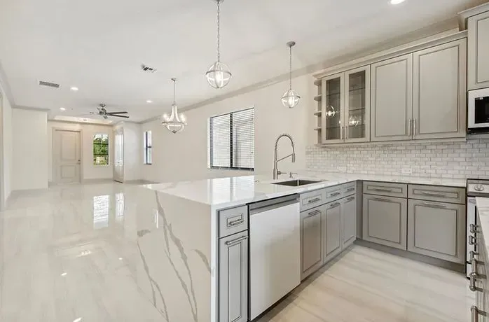 Bright modern kitchen with white cabinets, marble island, stainless appliances, and glossy tile floors