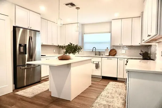 Bright modern white kitchen with stainless steel refrigerator, island, and wood floors