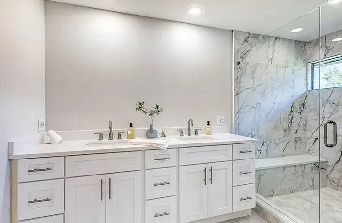 Modern white bathroom with double vanity, marble tile shower, and glass enclosure