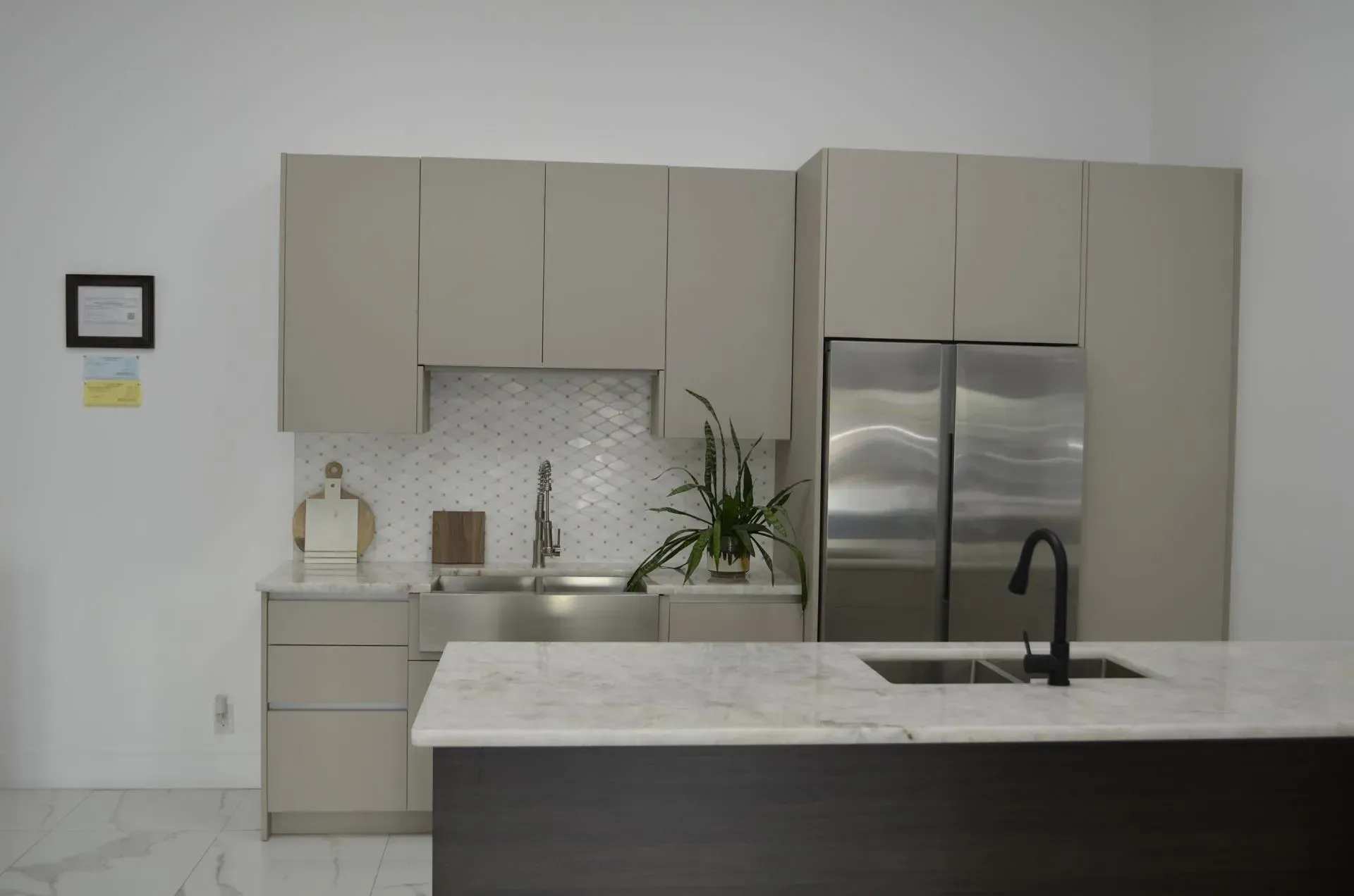 Modern kitchen with beige cabinets, stainless steel fridge, marble island, and black faucet