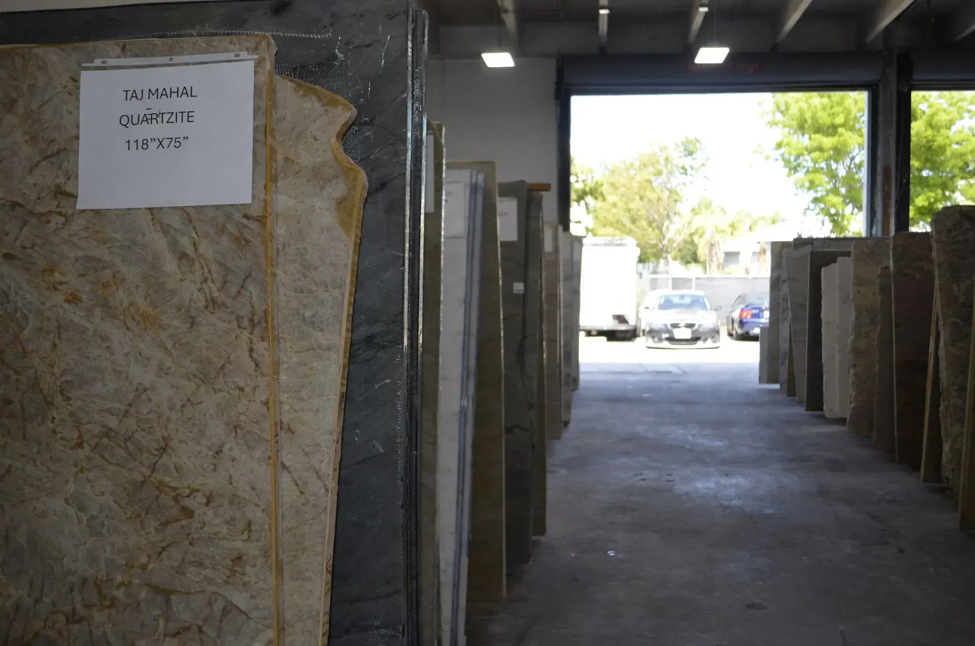 Covered walkway with large stone slabs and a bright exit to a parking lot outside.