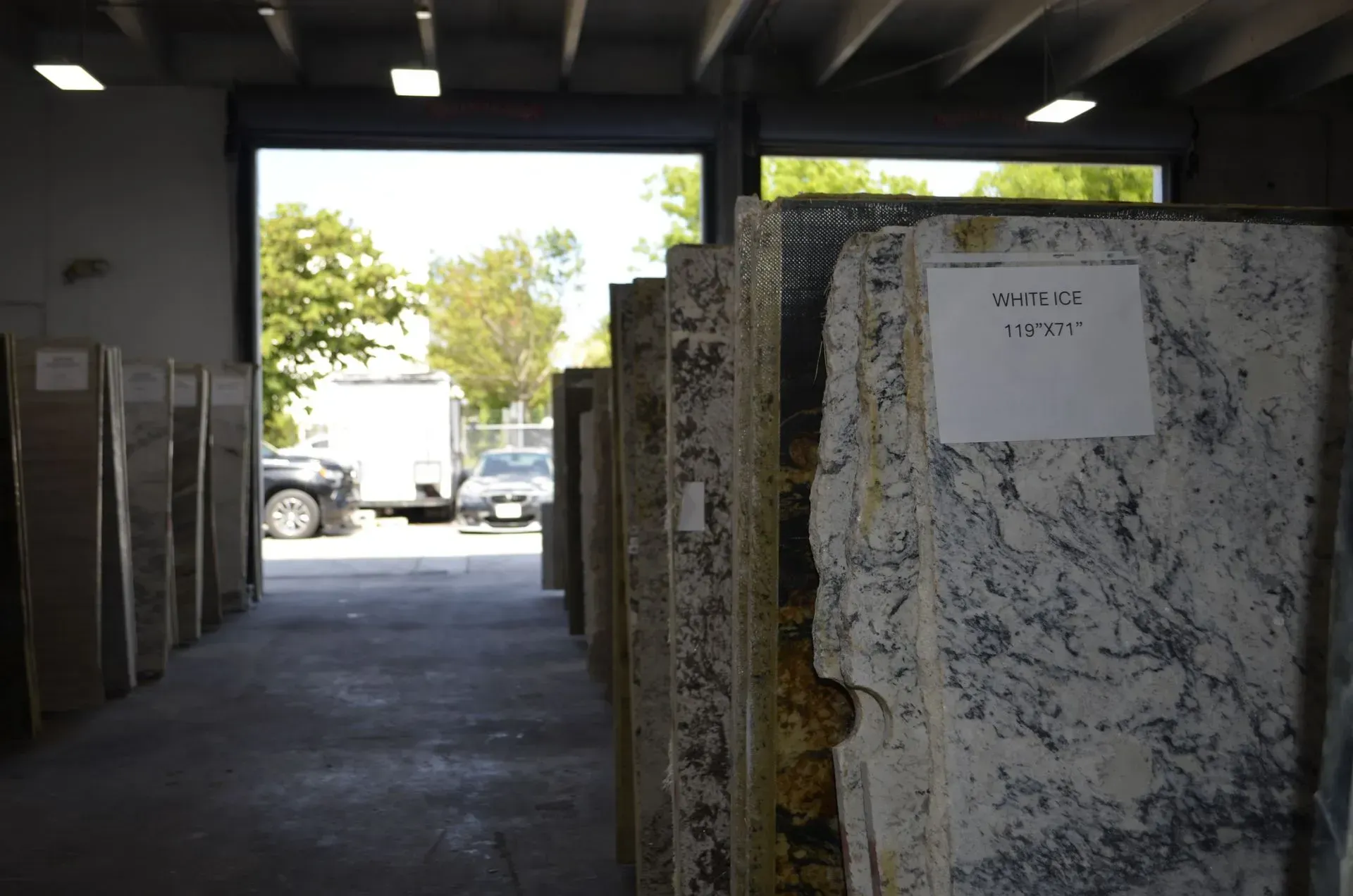 Stone slabs in a dim warehouse aisle, with a truck visible through the open doorway.