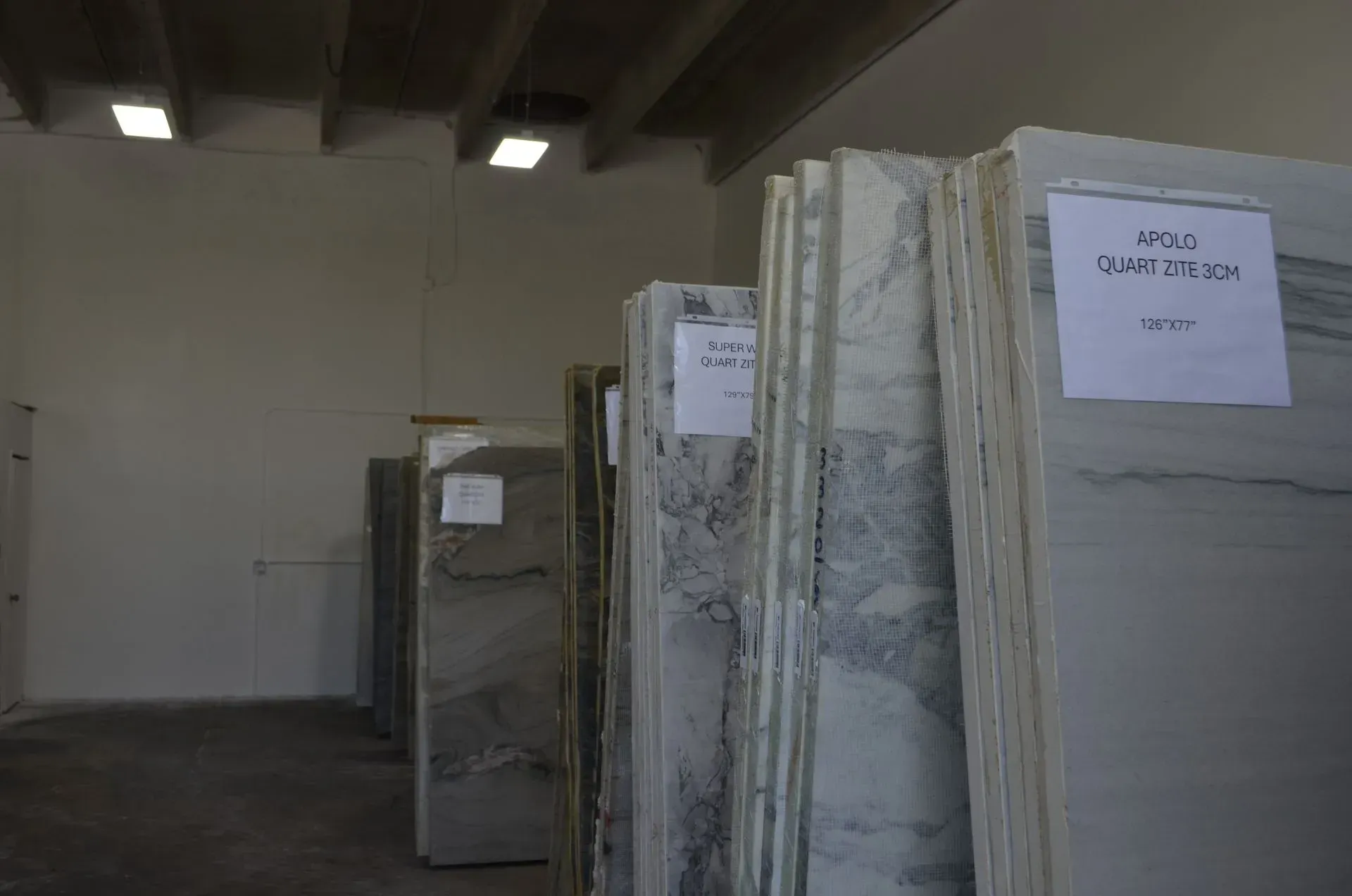 Large stone slabs stacked upright in an indoor warehouse aisle under fluorescent lights.