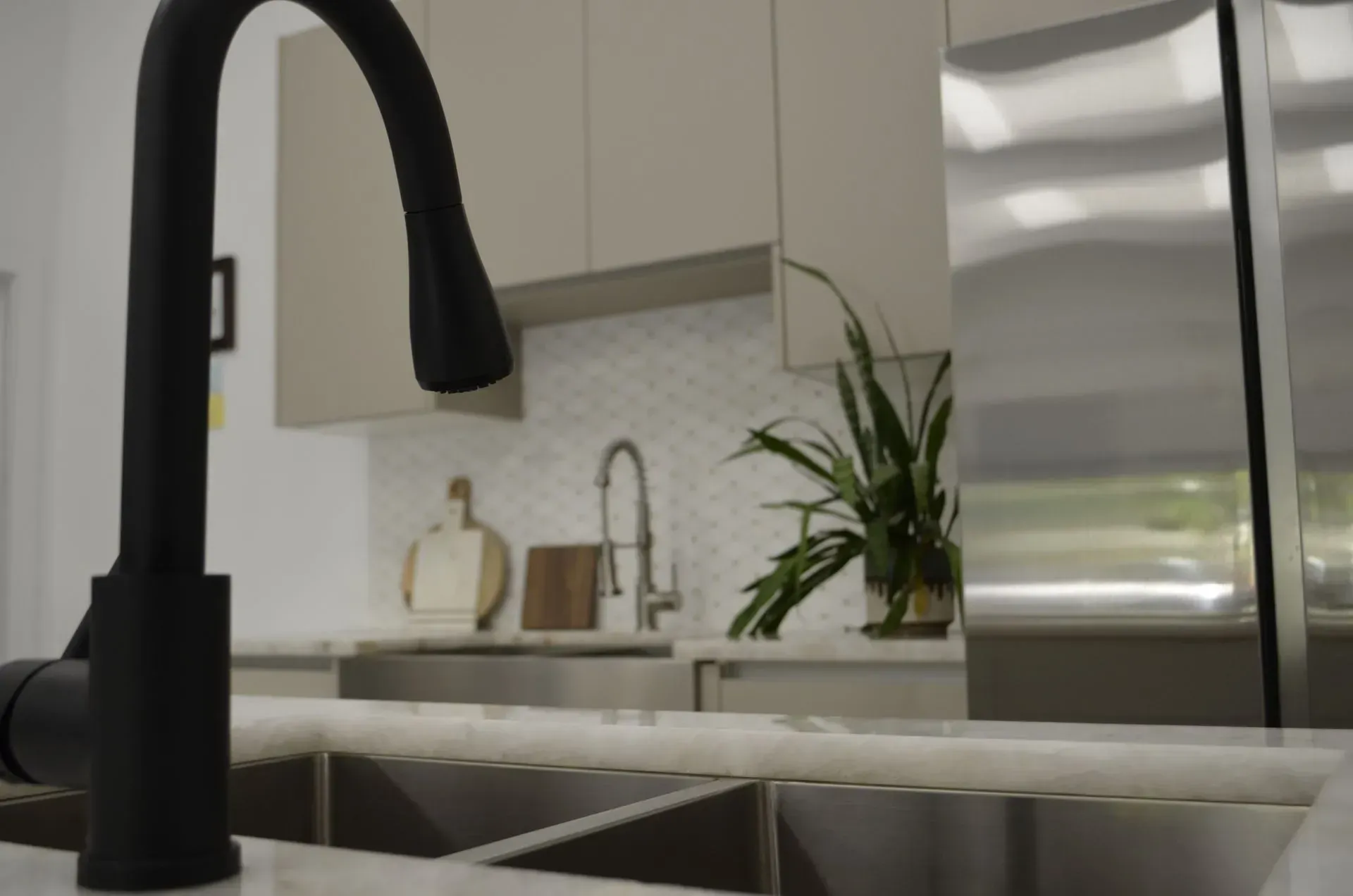 Modern kitchen sink with matte black faucet, white countertops, and stainless steel fridge in the background