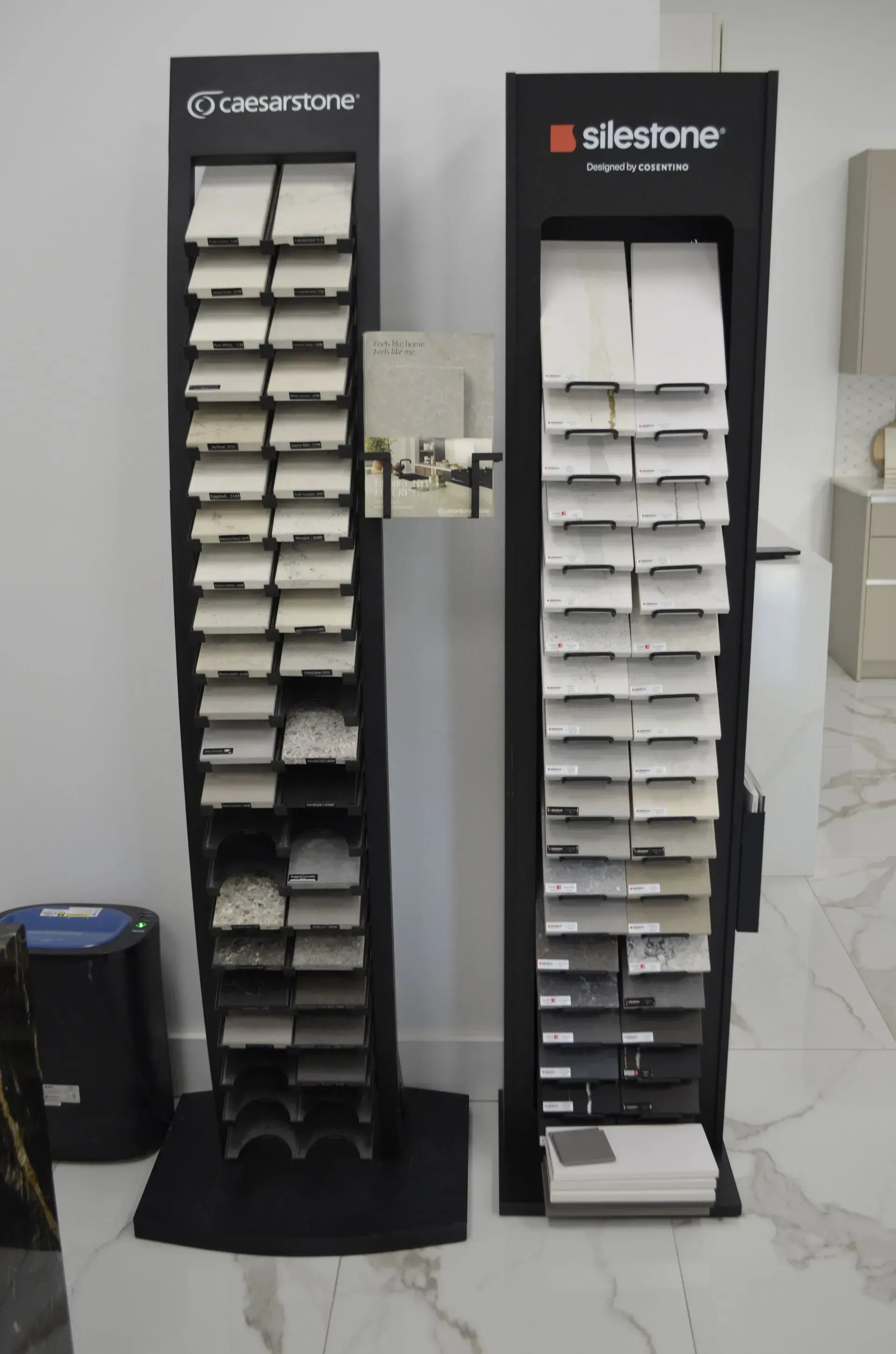 Two tall tile display racks with white sample tiles in a showroom, one branded Georgian and one Silestone.