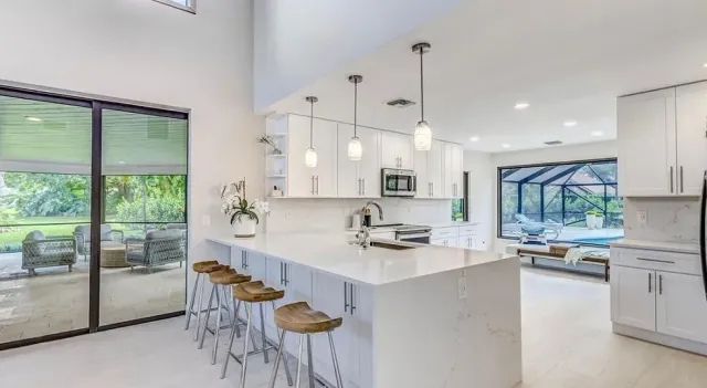 Bright modern kitchen with white island, bar stools, and large sliding glass doors overlooking greenery