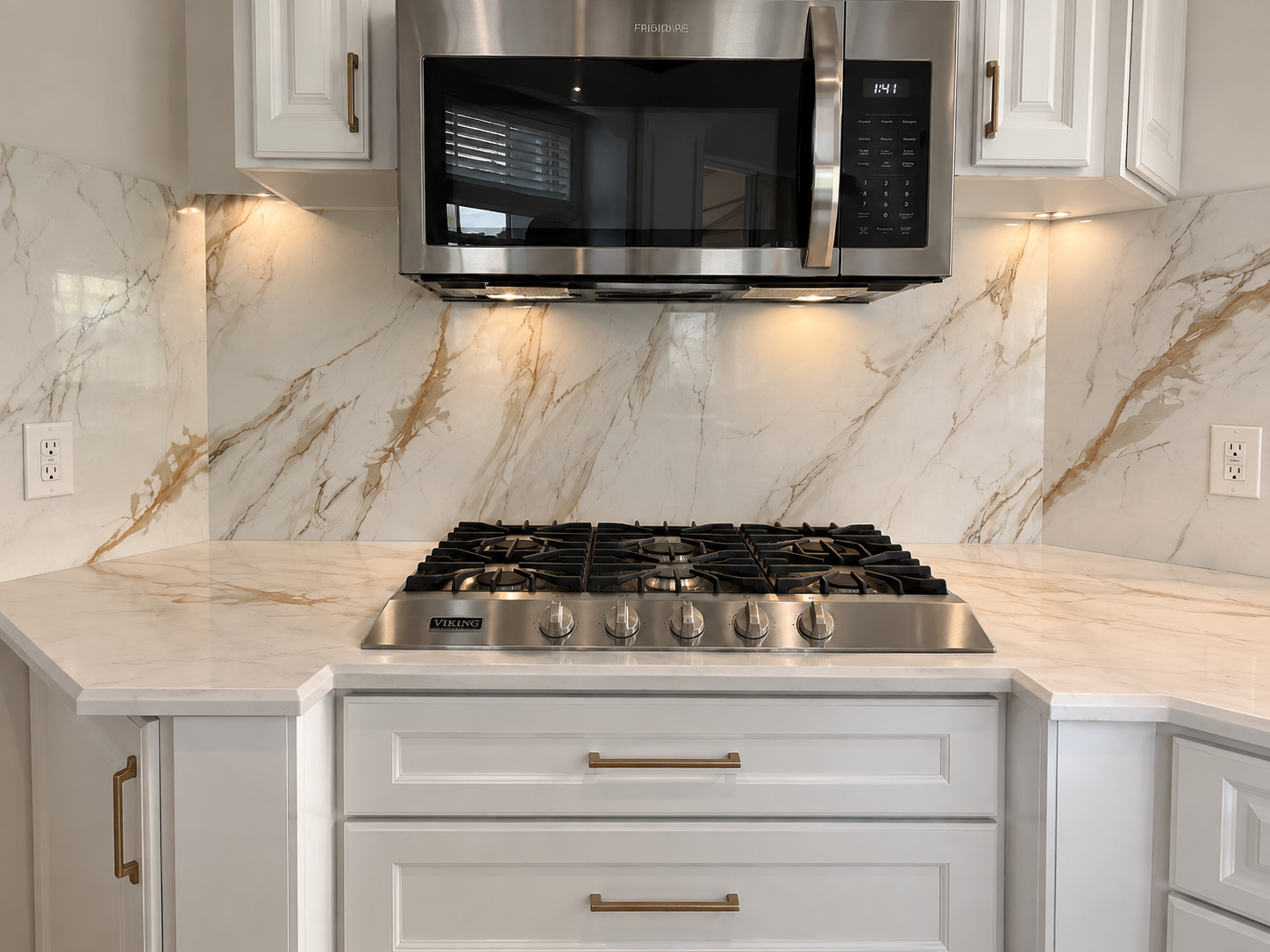 Modern white kitchen with marble backsplash, gas range, black microwave, and under-cabinet lighting