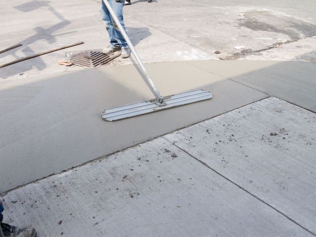 Wet concrete sidewalk being smoothed with a squeegee near a street drain.