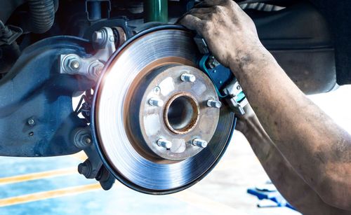 Mechanic replacing a car brake rotor and caliper on a lifted vehicle