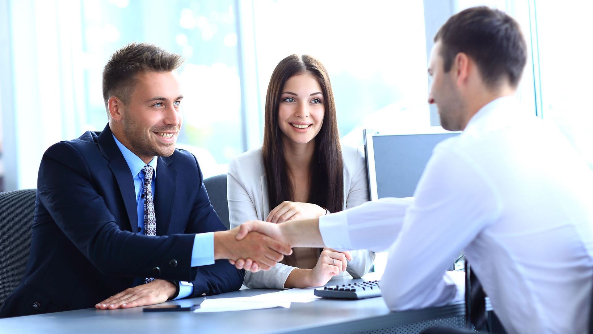 A man and a woman are shaking hands while sitting at a table.