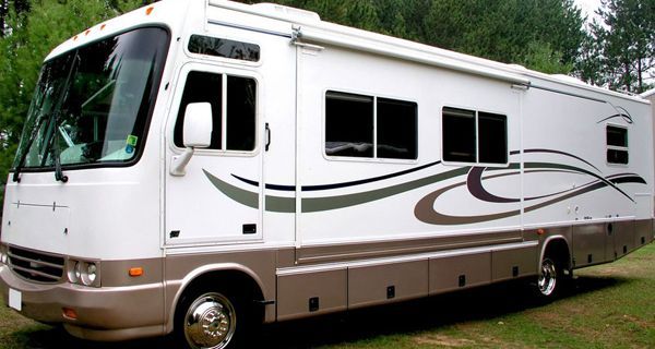 A large white and tan rv is parked in the grass