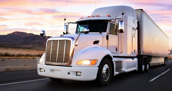 A white semi truck is driving down a highway at sunset.