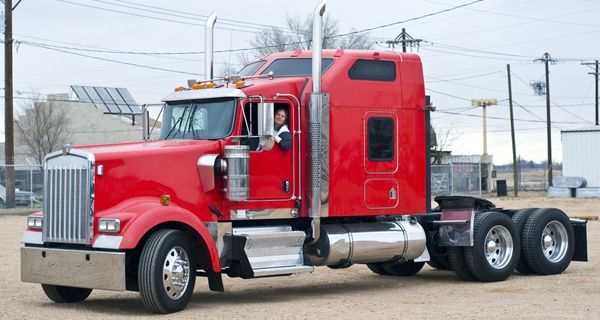 A red semi truck is parked in a dirt lot