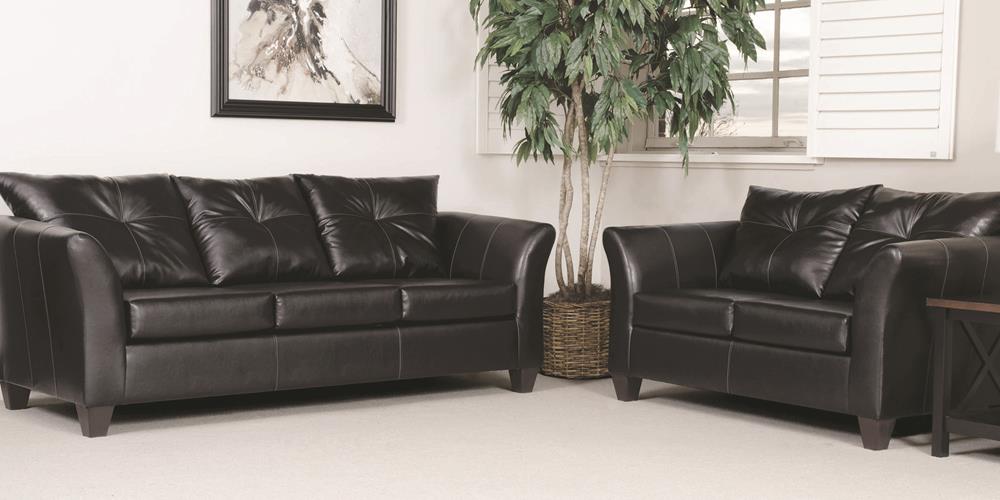 A living room with two black leather couches and a plant.