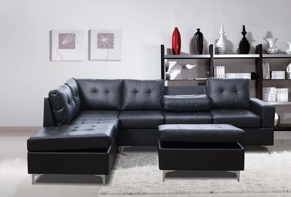 A living room with a black sectional couch and ottoman