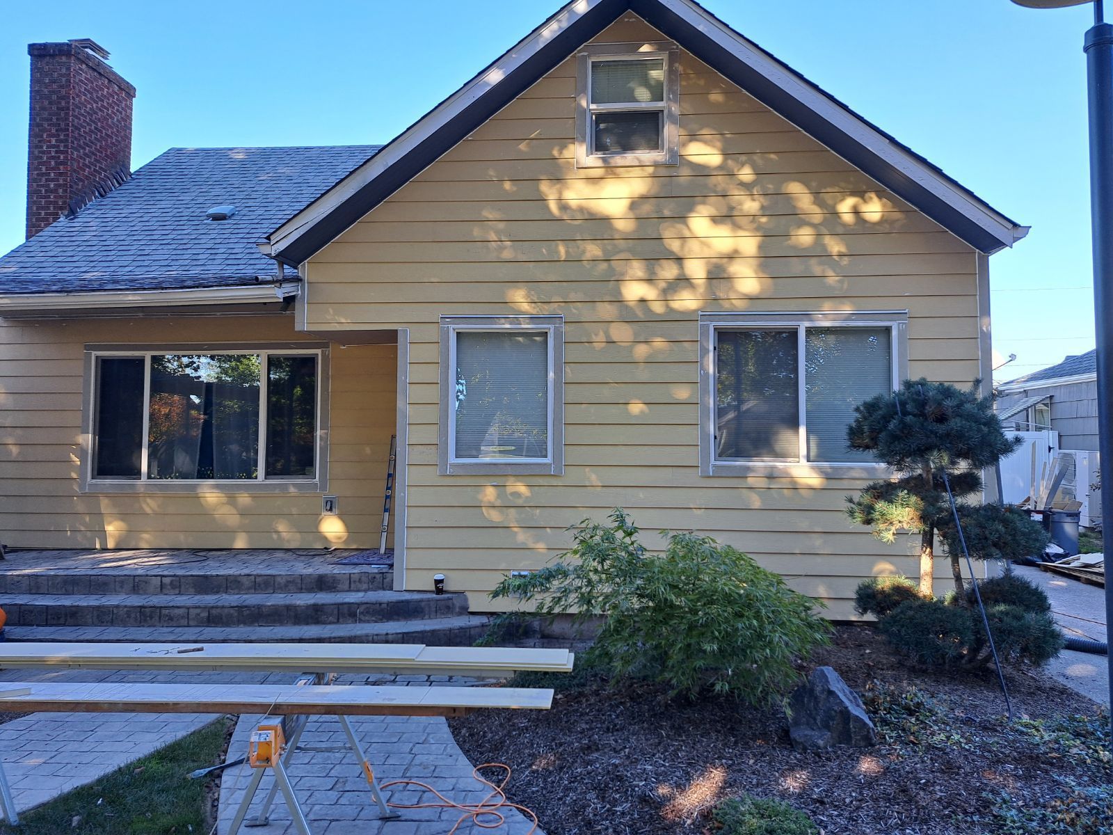A yellow, single-story house with a brick chimney and stone patio steps under construction on a sunny day.