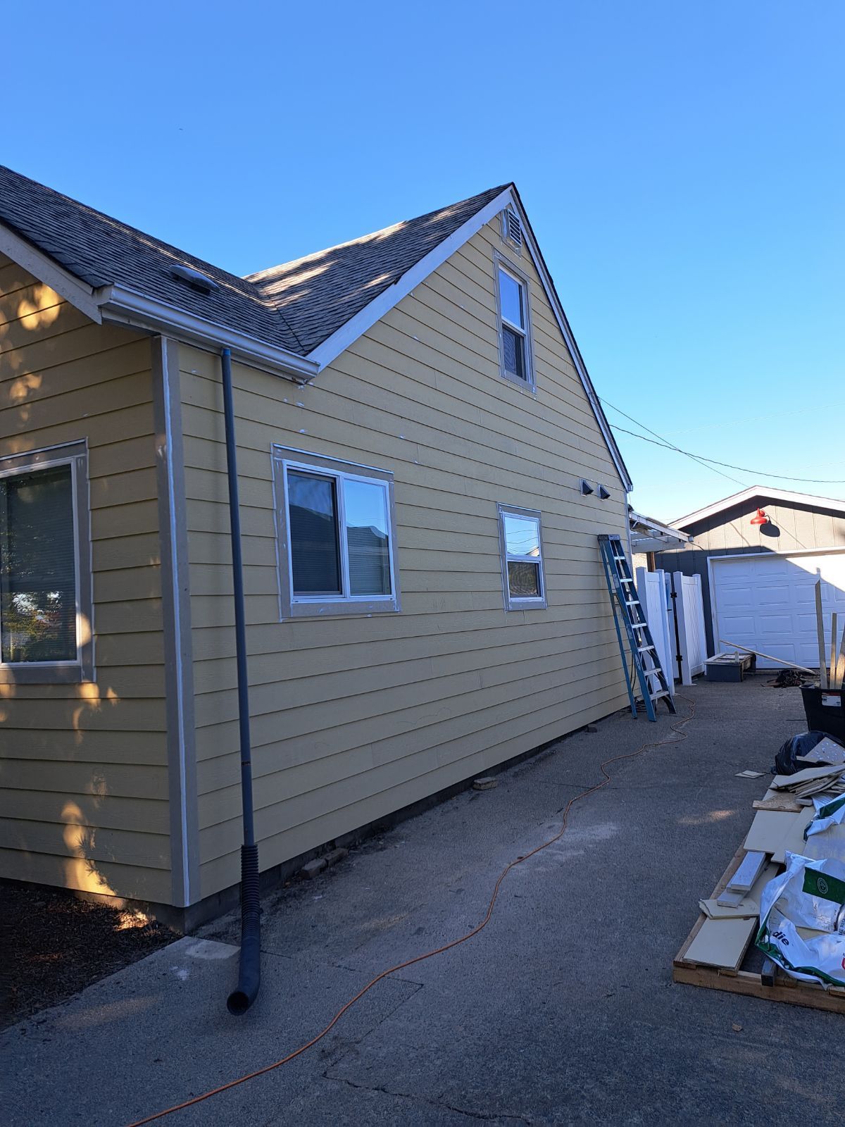 A side view of a yellow house with a gable roof, two windows, and a ladder leaning against the siding.