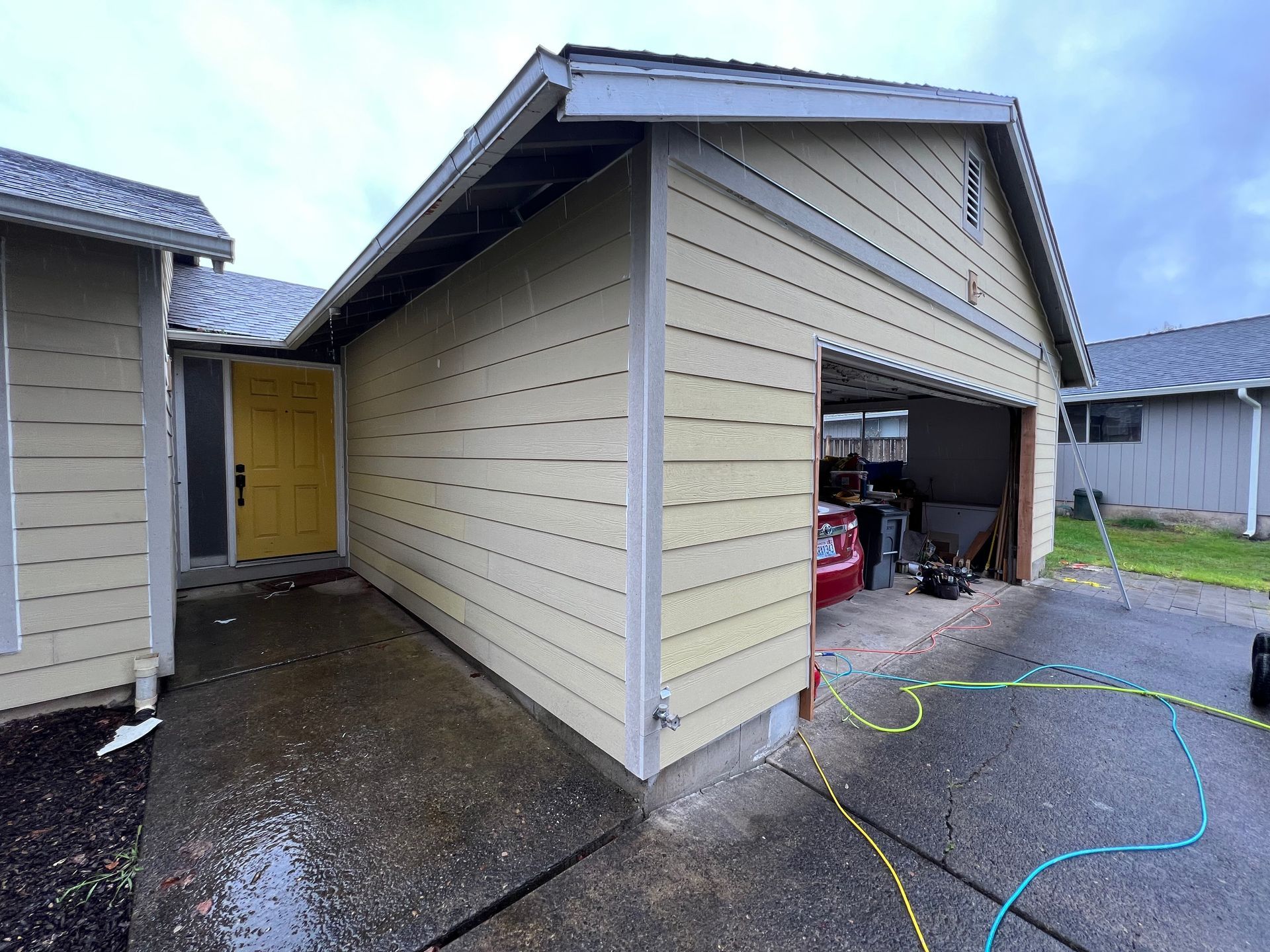 A beige house with a yellow front door and open garage, viewed from the driveway on an overcast day.