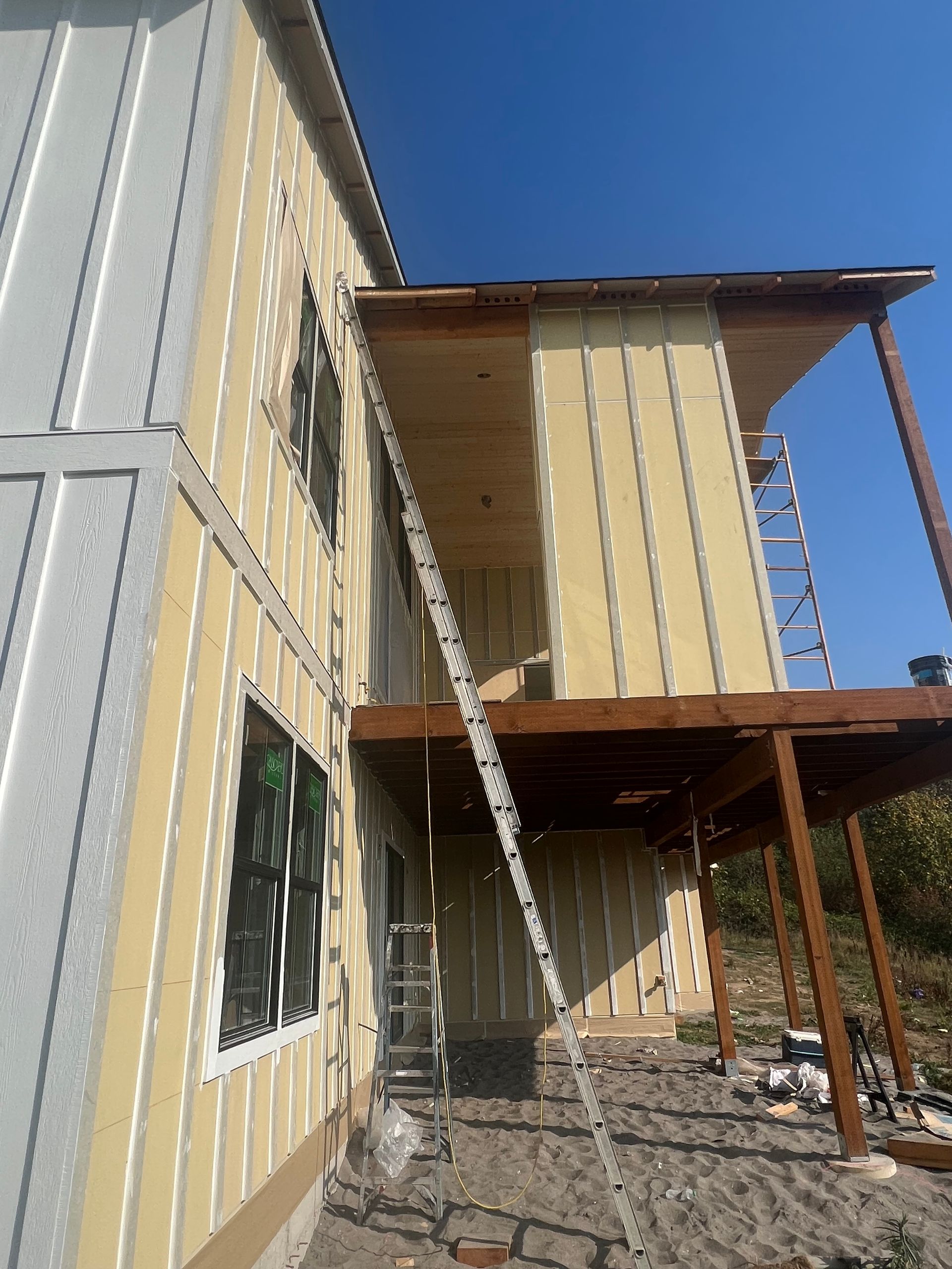 A multi-story building under construction with beige siding, exposed wood framing, and a long ladder leaning on the wall.