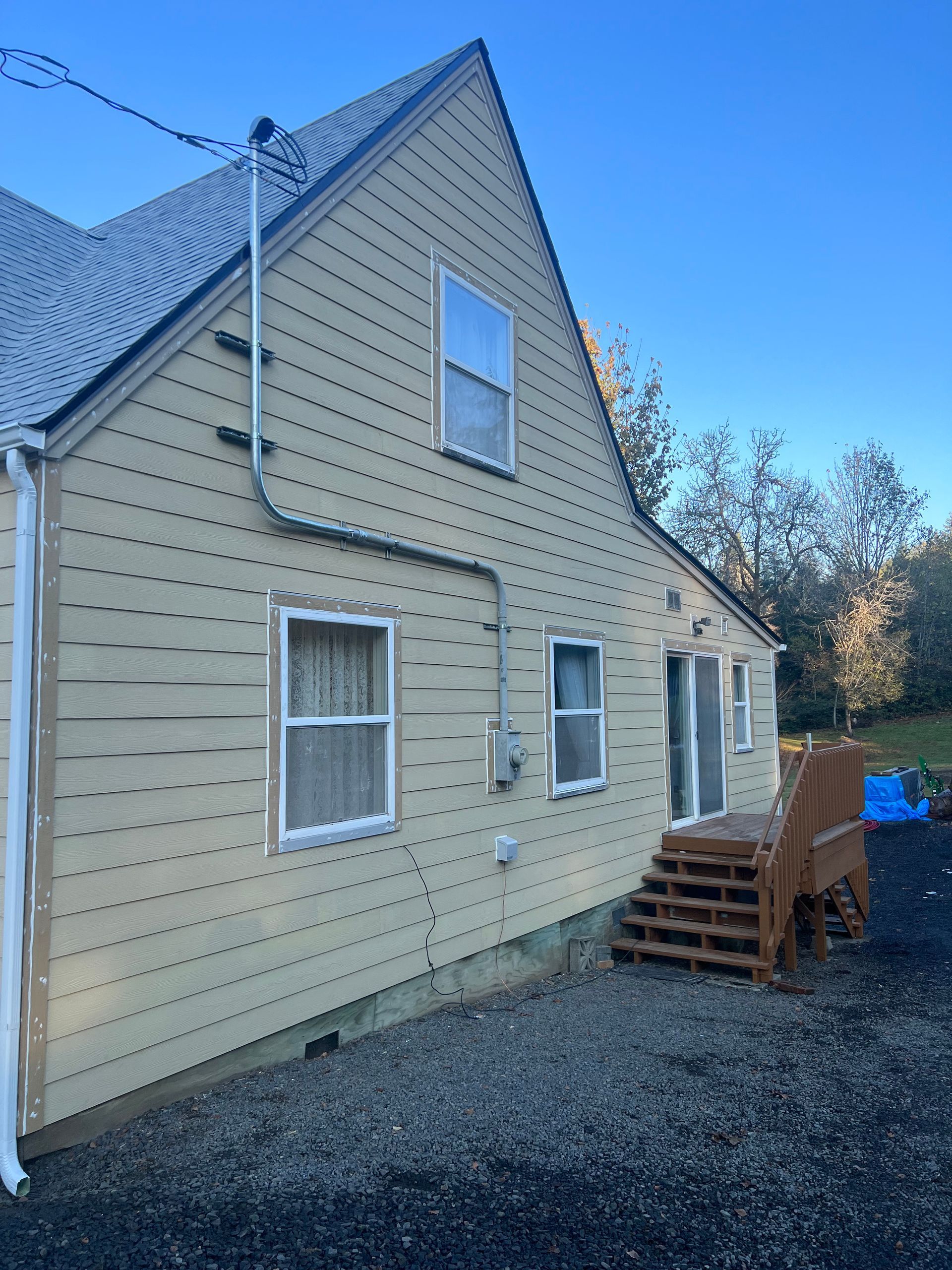 A light yellow house with lap siding, white-framed windows, and a set of wooden steps leading to a side door.