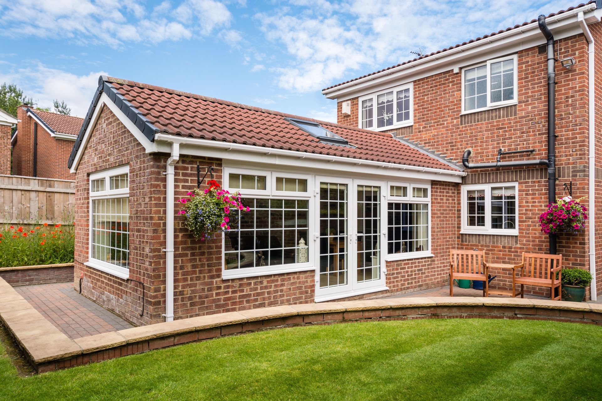 A red brick home extension with white-framed windows and French doors, leading to a landscaped garden and patio.
