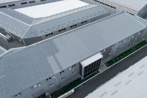Aerial view of a large gray industrial building with a corrugated roof and central entrance.