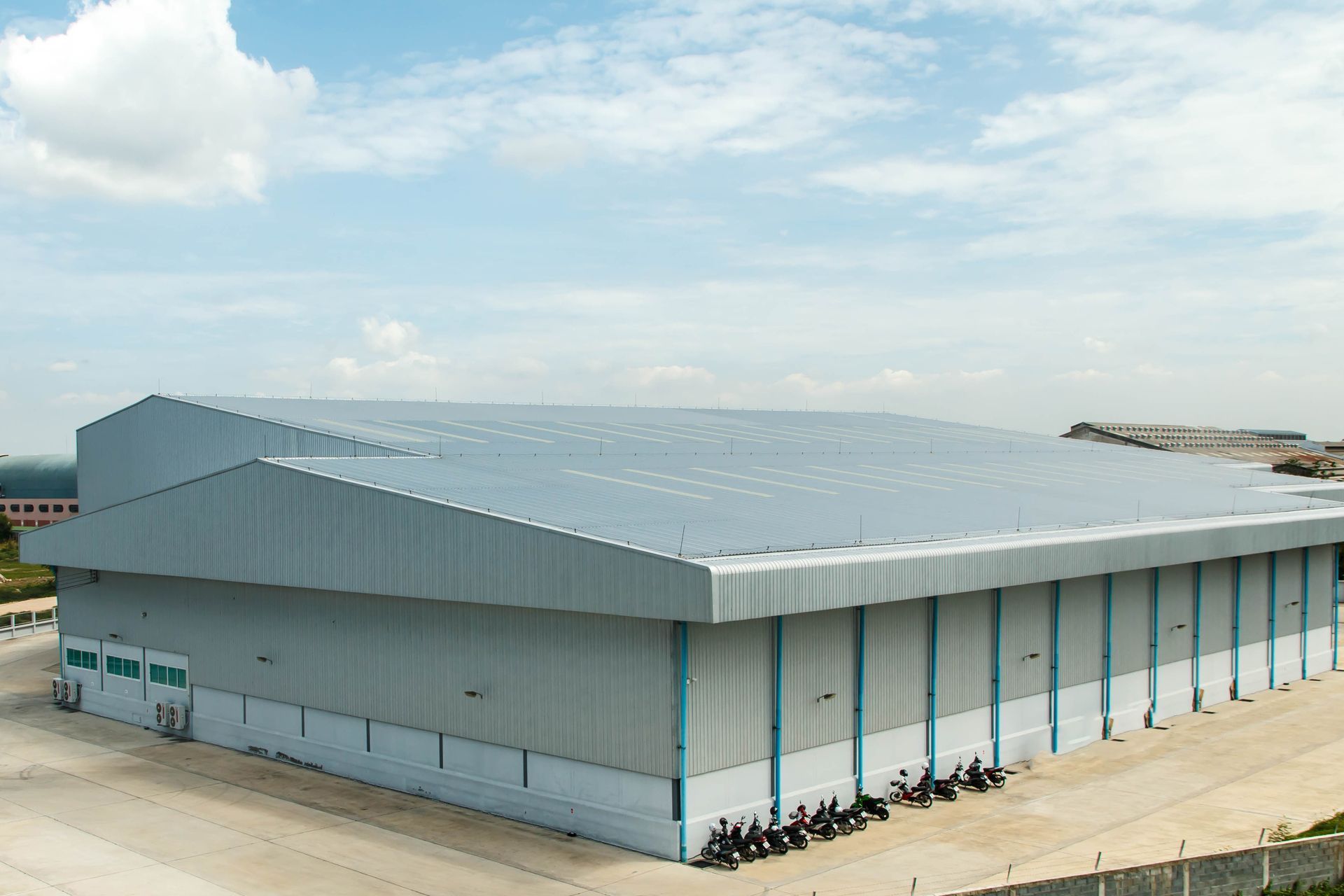 Large gray industrial warehouse beside water under a partly cloudy sky