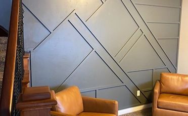 Geometric accent wall with two brown leather armchairs; next to staircase.