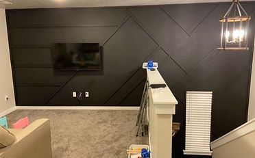 Black accent wall with geometric wood paneling, TV, and staircase.