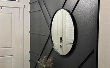Dark gray accent wall with an oval mirror. Next to a white door.