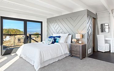Bedroom with white bed, geometric gray accent wall, large windows with a view.