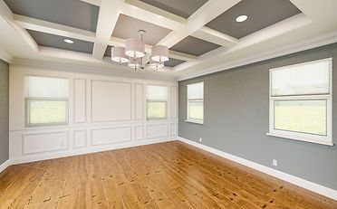 Empty room with gray walls, white trim, wood floor, and coffered ceiling with chandelier.