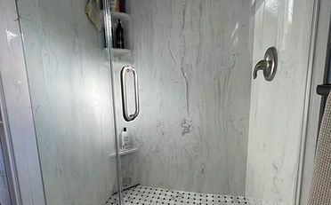 Shower stall with marble-like walls, a glass door, and a tiled floor. Contains shampoo and soap.