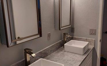 Bathroom with two sinks, mirrors, gray countertop and walls; silver fixtures, white square sinks.