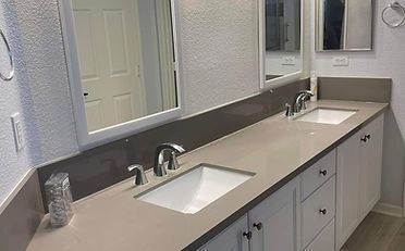 Bathroom with dual sinks, white cabinets, beige countertop, grey backsplash, and large mirrors.