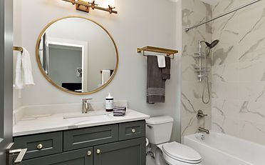 Bathroom with dark green vanity, gold accents, round mirror, and marble shower surround.