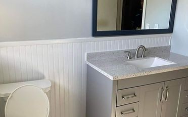 Bathroom with a gray vanity, white beadboard, and a dark-framed mirror.