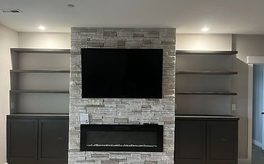 Living room with a fireplace, TV, built-in shelves, and dark cabinets. The central feature is a stone accent wall.