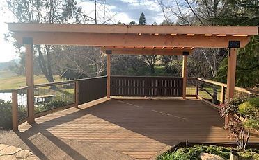Wooden deck with pergola overlooking a landscape with trees and greenery.
