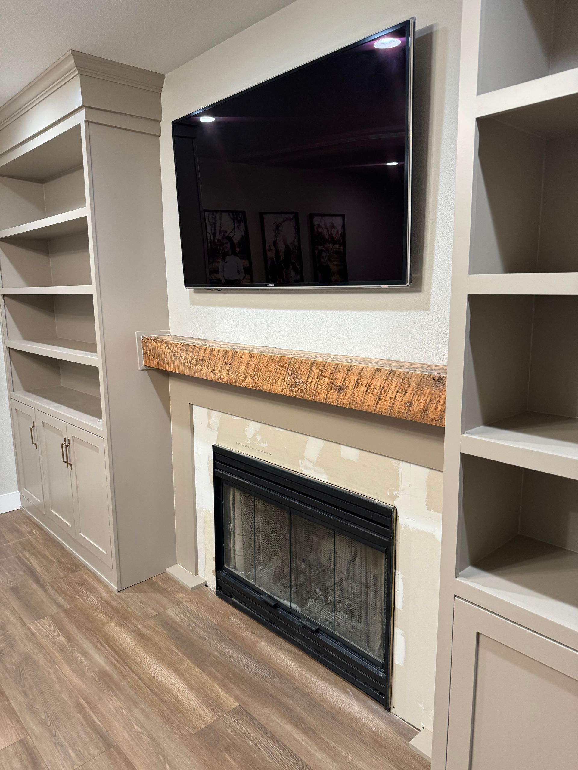 Fireplace with TV above, flanked by built-in bookshelves. Beige walls, wood mantel, and light wood-look flooring.