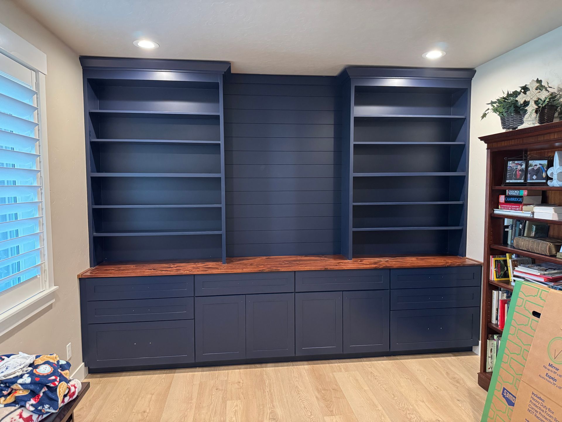 Built-in navy blue bookshelves, cabinets, and desk with wood top against a white wall.
