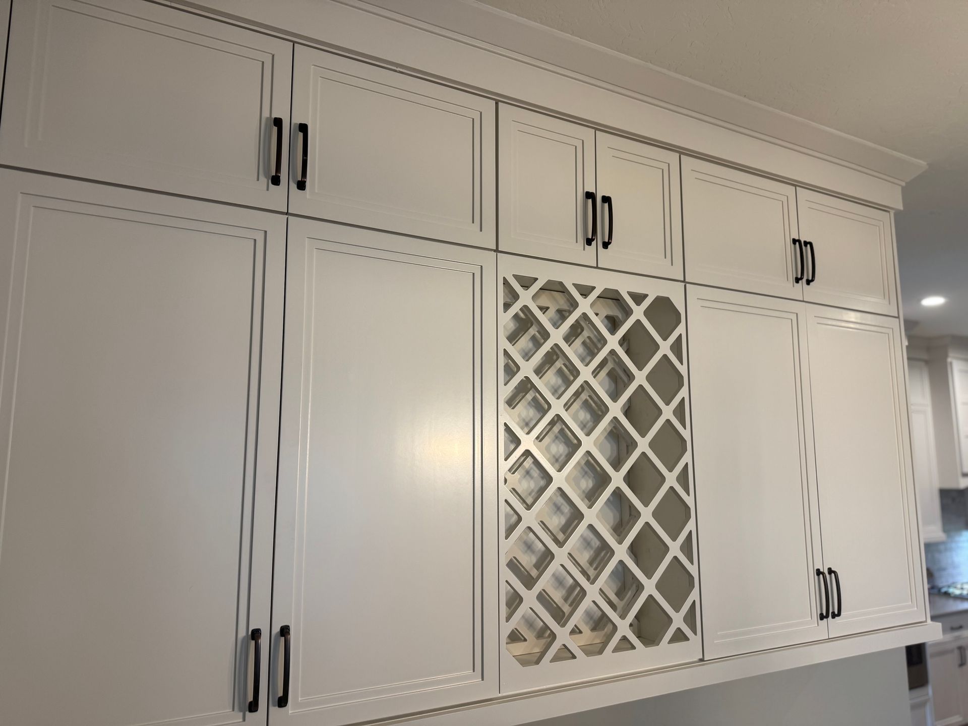 White kitchen cabinets with black handles and a built-in wine rack.