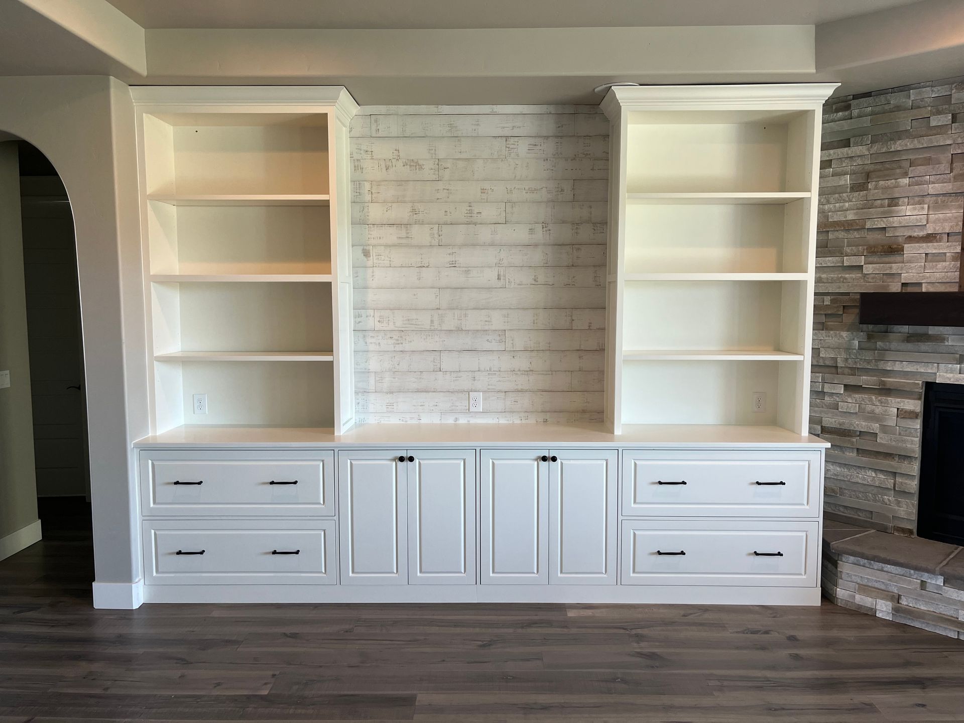 White built-in shelving unit with bookshelves, cabinets, and drawers, against a white-washed brick wall and fireplace.