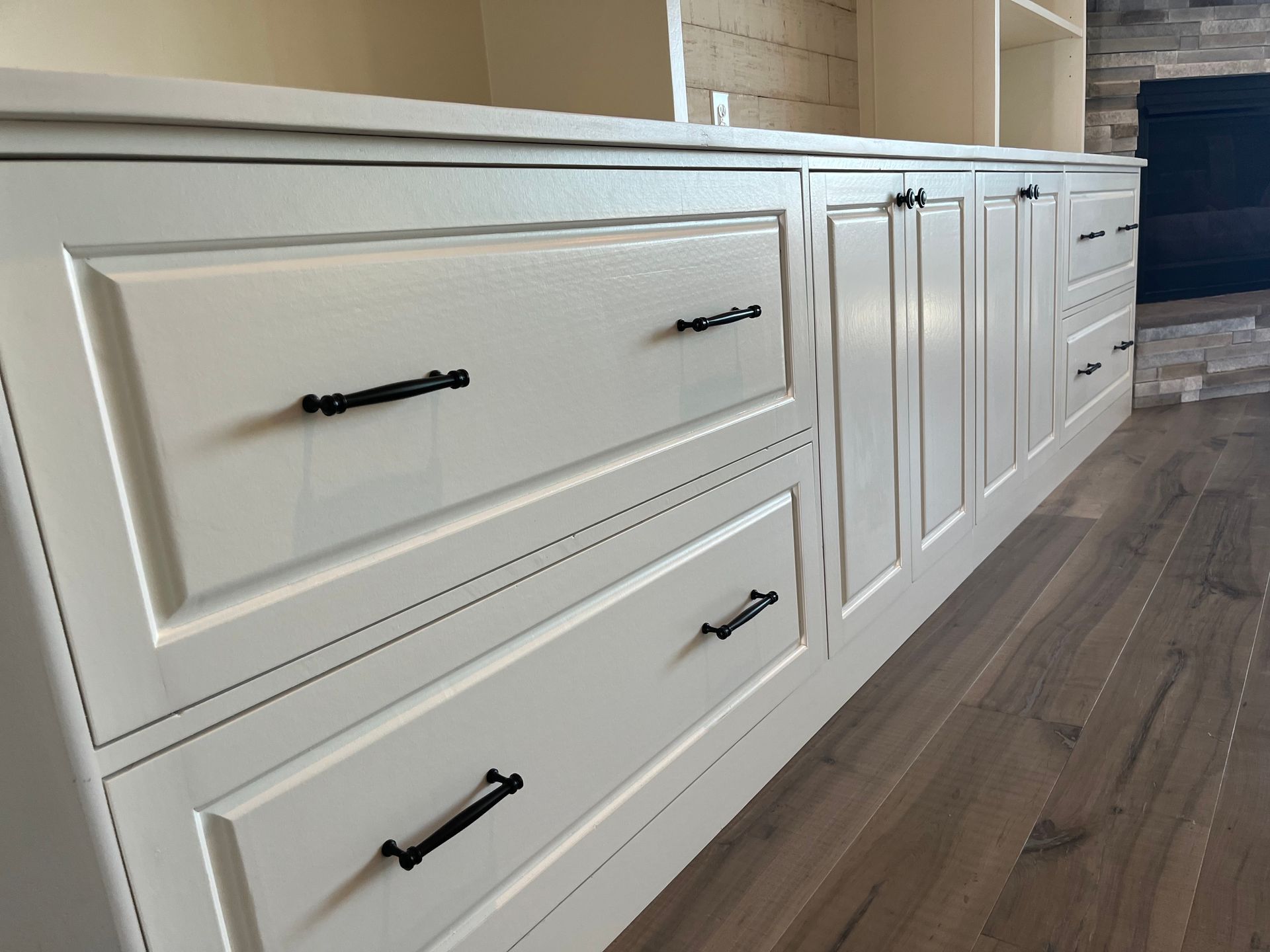 White cabinets with black handles, drawers, and doors, set against a wooden floor.