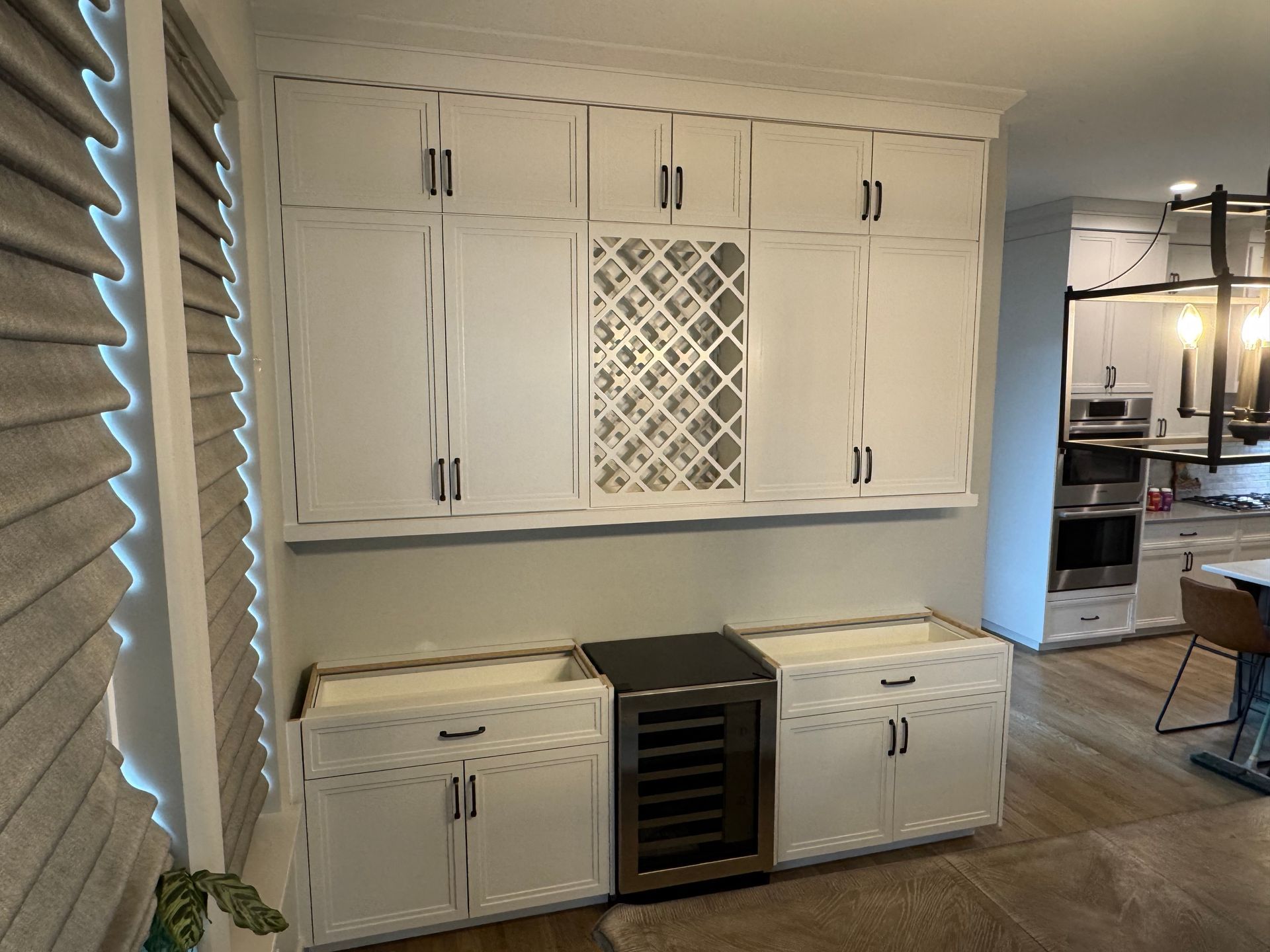 White cabinets with black hardware; wine rack; wine fridge. Kitchen setting.