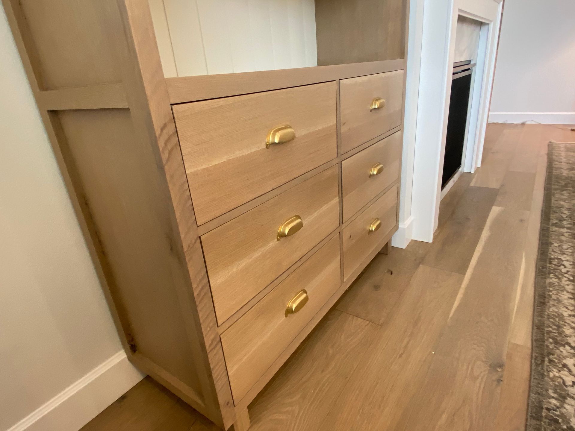Wooden cabinet with six drawers and gold handles, in a room with wood flooring.