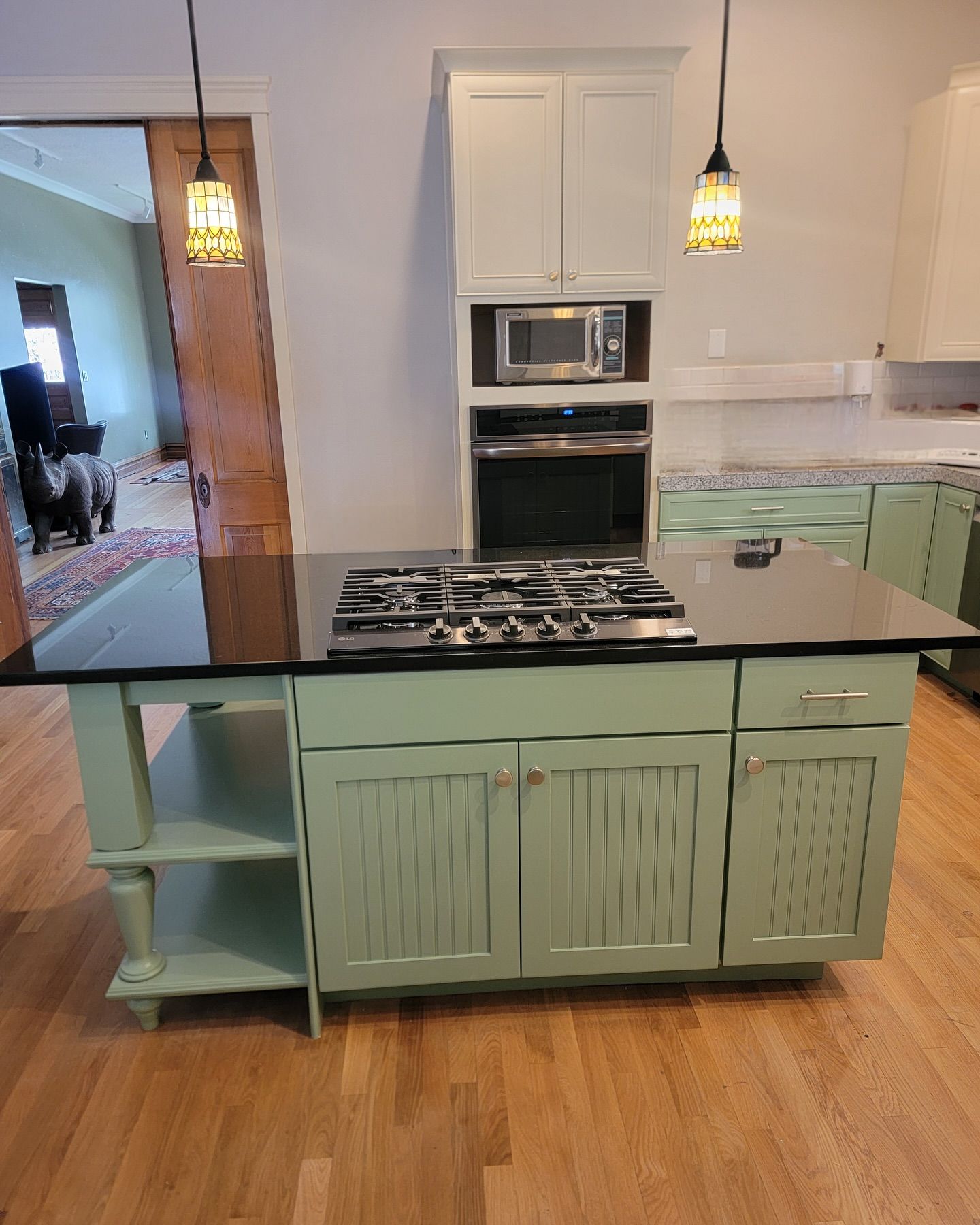 Kitchen island with green cabinets, black countertop, and stovetop. A light-colored wood floor.